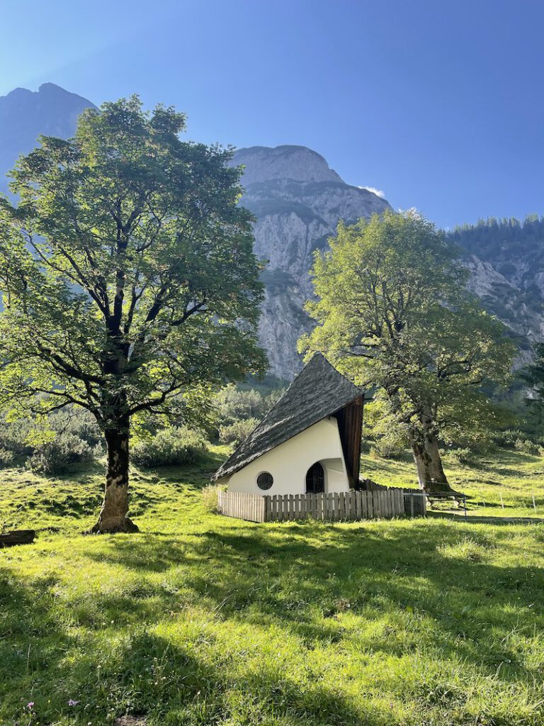 Bergkapelle zwischen zwei Bäumen vorm Karwendel-Bergmassiv, Symbol für Neuanfang und Seelenreise