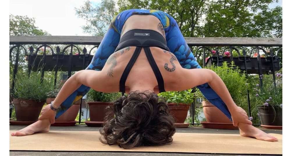 Frau in weiter Vorbeuge-Yogapose auf einem Balkon mit grünem Hintergrund