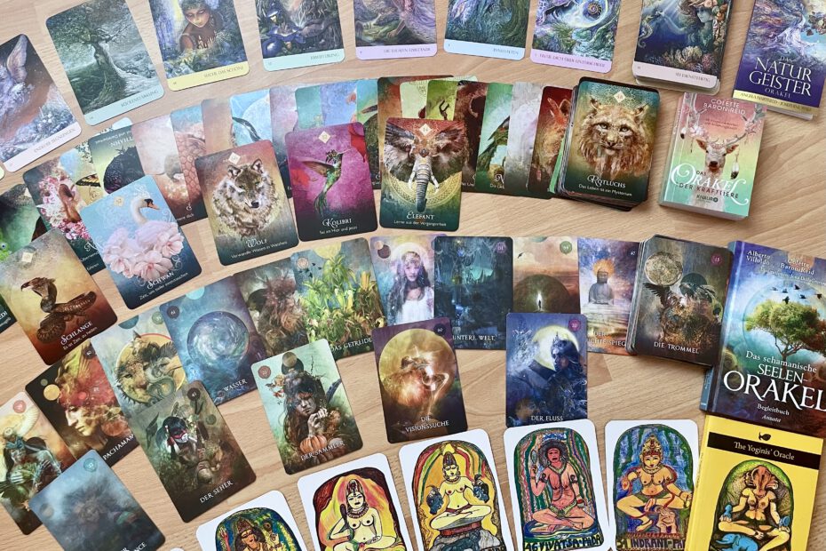 Orakelkarten aus verschiedenen spirituellen Decks – Naturgeister, Krafttiere, schamanische Symbole und Yoginis – auf Holz ausgebreitet