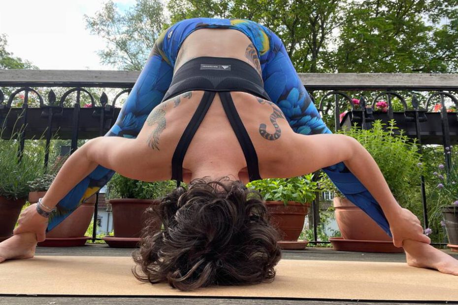 Frau in weiter Vorbeuge-Yogapose auf einem Balkon mit grünem Hintergrund